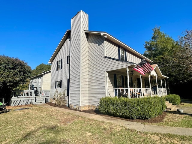 view of side of property featuring a porch, ceiling fan, and a lawn