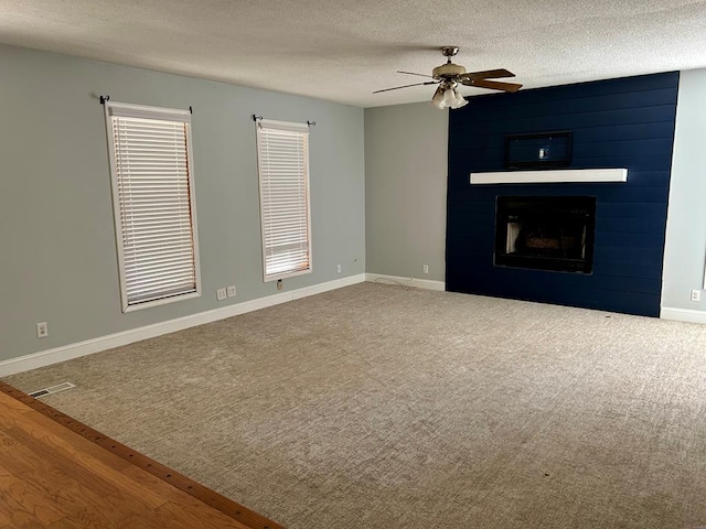 unfurnished living room with a textured ceiling, ceiling fan, carpet floors, and a fireplace