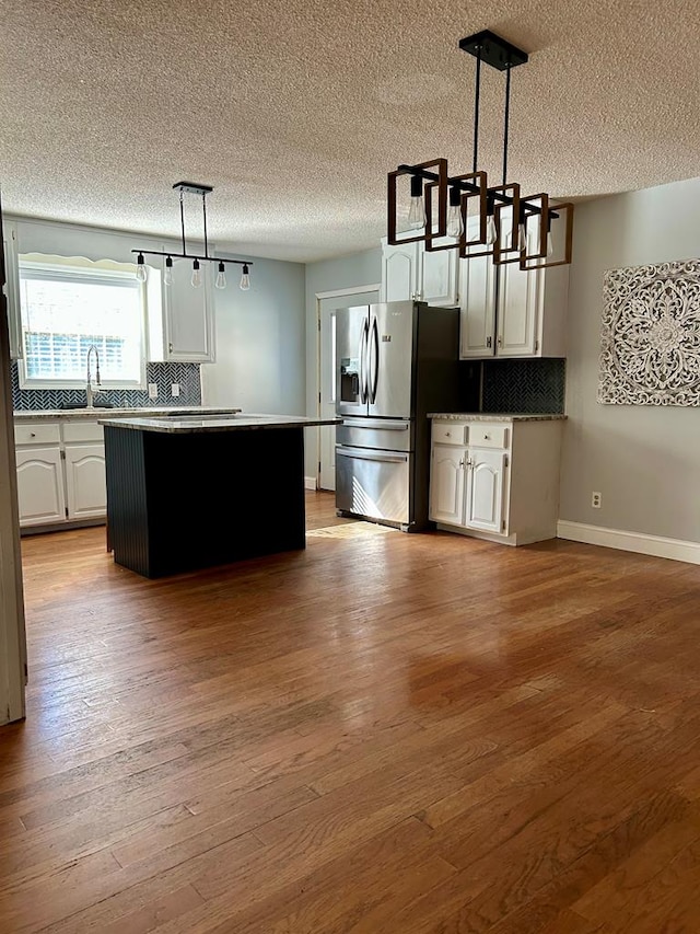 kitchen with light wood-type flooring, pendant lighting, stainless steel fridge with ice dispenser, a center island, and white cabinetry