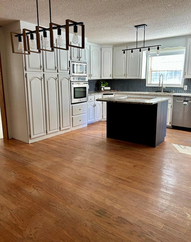 kitchen featuring hanging light fixtures, stainless steel appliances, light hardwood / wood-style flooring, decorative backsplash, and a kitchen island