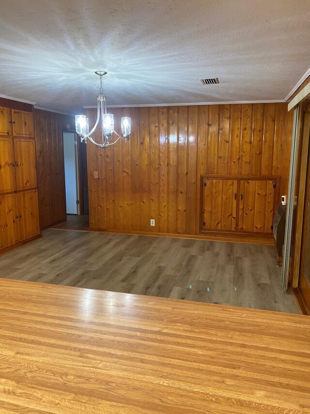 unfurnished dining area featuring hardwood / wood-style flooring, wood walls, a textured ceiling, and an inviting chandelier