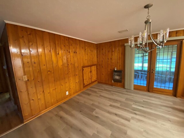 unfurnished dining area featuring hardwood / wood-style floors, wood walls, a chandelier, ornamental molding, and heating unit