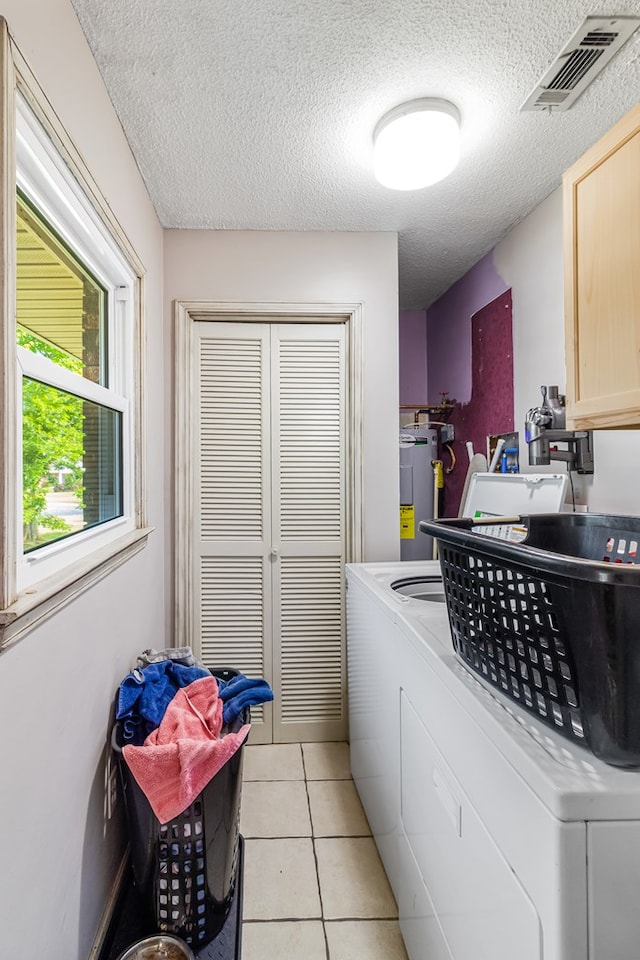 clothes washing area featuring washing machine and clothes dryer, cabinets, water heater, a textured ceiling, and light tile patterned floors