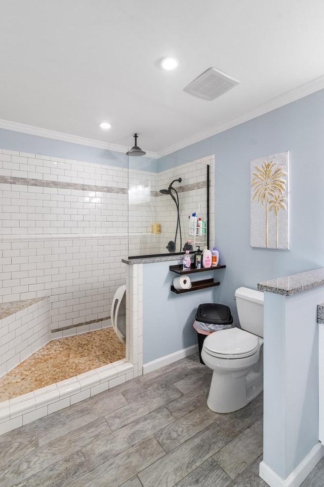 bathroom with toilet, ornamental molding, and tiled shower