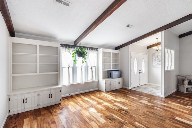 unfurnished living room with beamed ceiling, a textured ceiling, light hardwood / wood-style floors, and an inviting chandelier