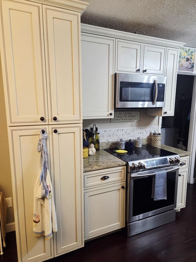 kitchen featuring light stone counters, appliances with stainless steel finishes, dark wood-style floors, cream cabinetry, and a textured ceiling