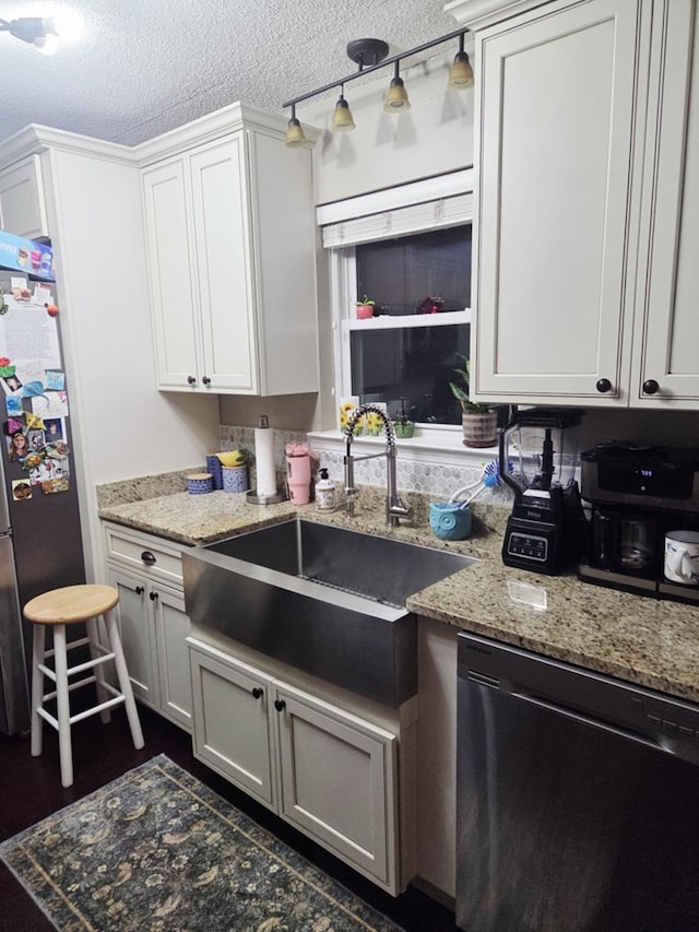 kitchen featuring light stone counters, dishwashing machine, freestanding refrigerator, a textured ceiling, and a sink