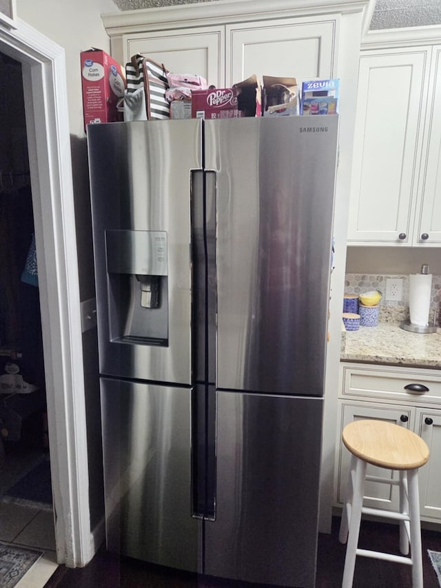 kitchen featuring light stone counters, white cabinetry, and stainless steel refrigerator with ice dispenser