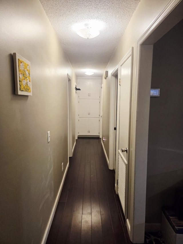 corridor featuring baseboards, a textured ceiling, and dark wood finished floors