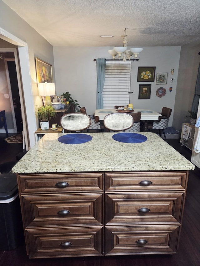 kitchen with a center island, a chandelier, dark brown cabinetry, light stone counters, and a textured ceiling