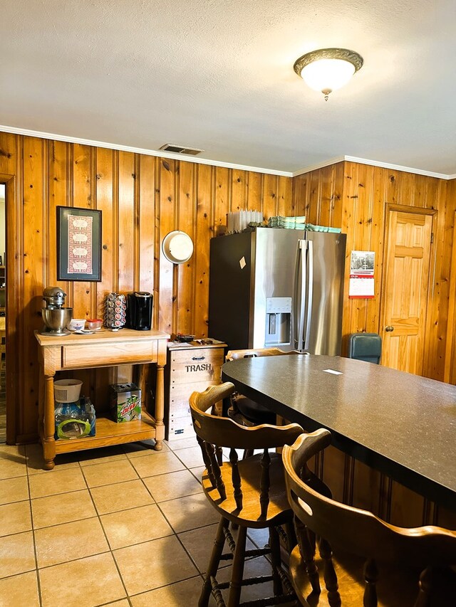 kitchen featuring crown molding, wood walls, light tile patterned floors, and stainless steel refrigerator with ice dispenser