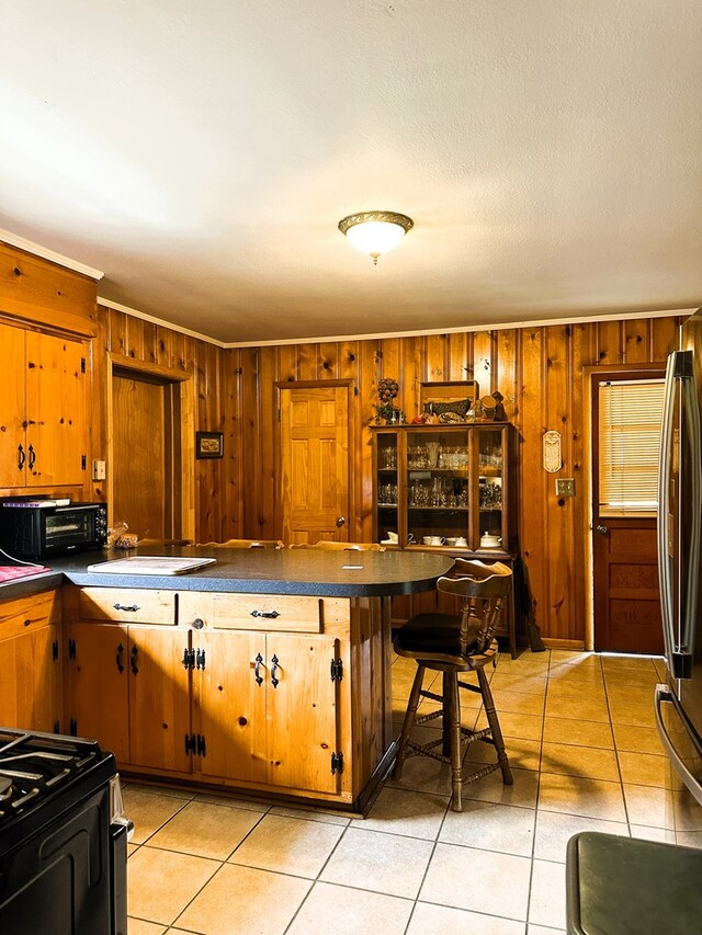 kitchen with a kitchen breakfast bar, stainless steel refrigerator, wooden walls, and light tile patterned floors