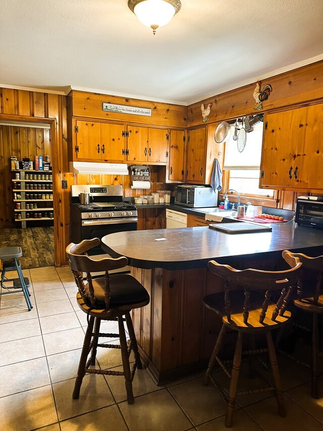 kitchen featuring gas range, wood walls, kitchen peninsula, and light tile patterned floors