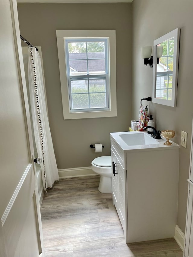 full bathroom featuring toilet, vanity, a healthy amount of sunlight, and wood-type flooring