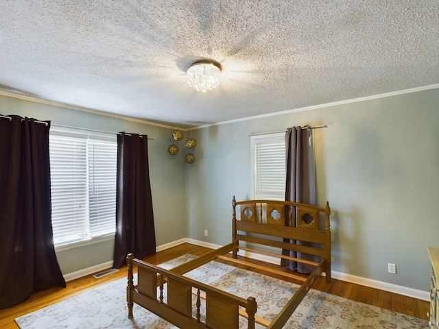 bedroom featuring ornamental molding, wood finished floors, visible vents, and baseboards