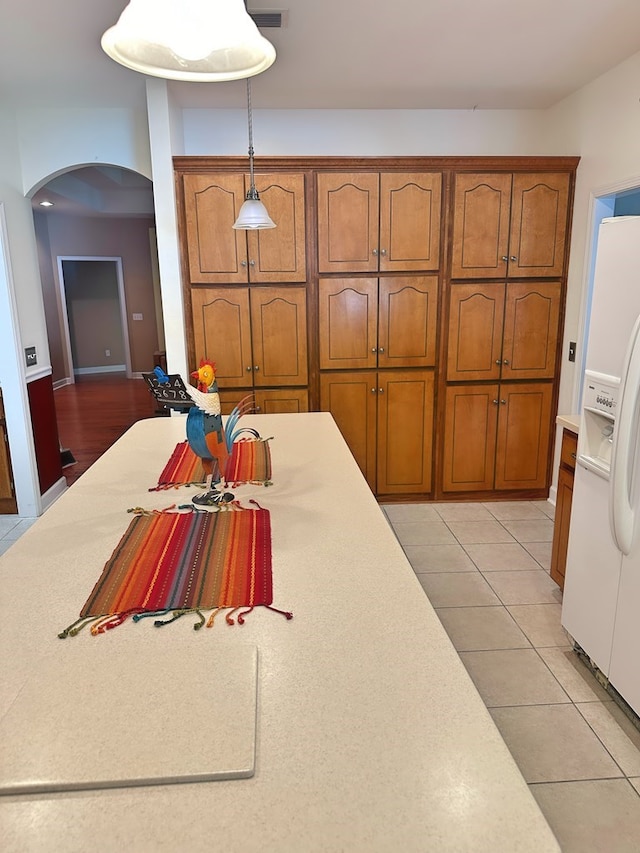 kitchen featuring light countertops, decorative light fixtures, arched walkways, and brown cabinets