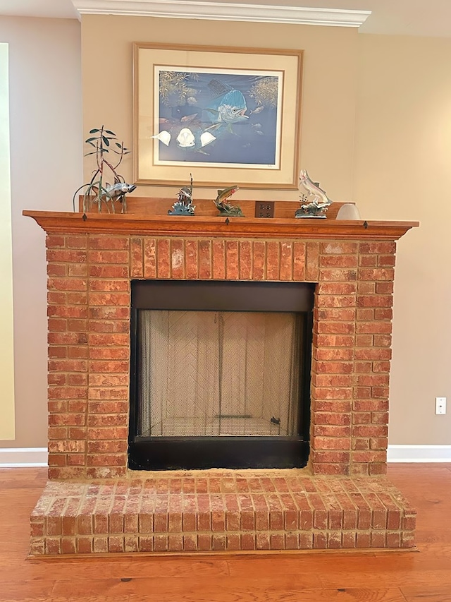 room details featuring ornamental molding, a brick fireplace, baseboards, and wood finished floors