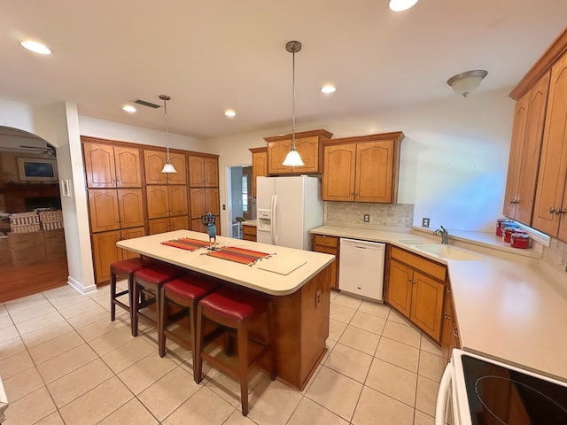 kitchen with a kitchen island, light countertops, decorative backsplash, white appliances, and a sink