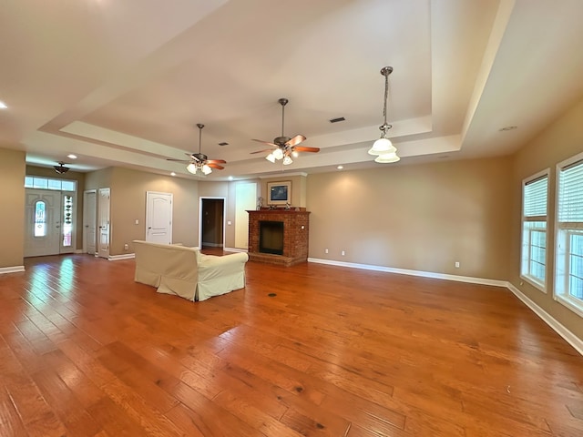 unfurnished living room with a tray ceiling, hardwood / wood-style flooring, a fireplace, and a healthy amount of sunlight