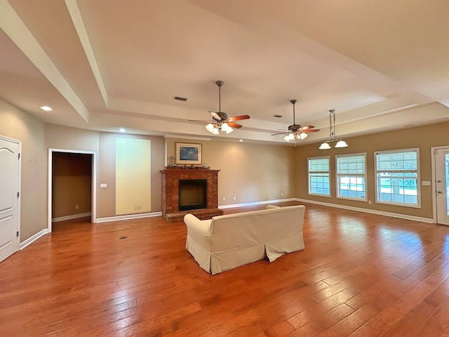 unfurnished living room featuring a raised ceiling, a brick fireplace, hardwood / wood-style flooring, and baseboards