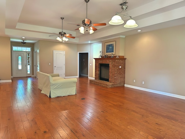 unfurnished living room with visible vents, a brick fireplace, baseboards, hardwood / wood-style floors, and a raised ceiling