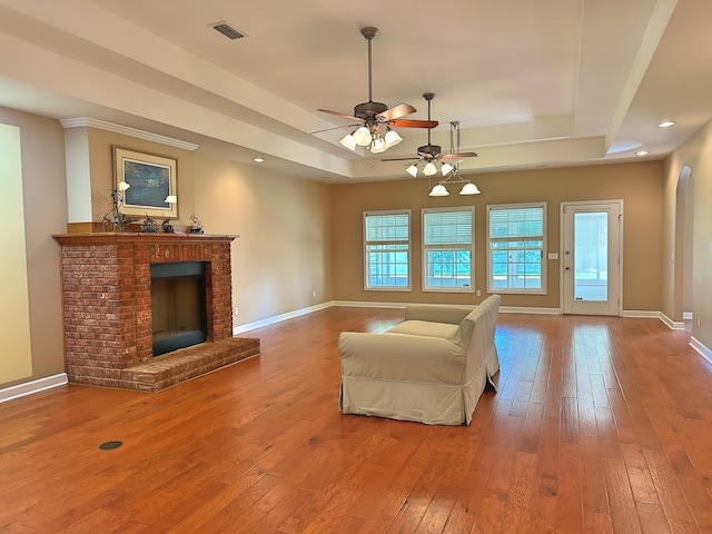 unfurnished living room featuring hardwood / wood-style floors, baseboards, visible vents, a tray ceiling, and a brick fireplace