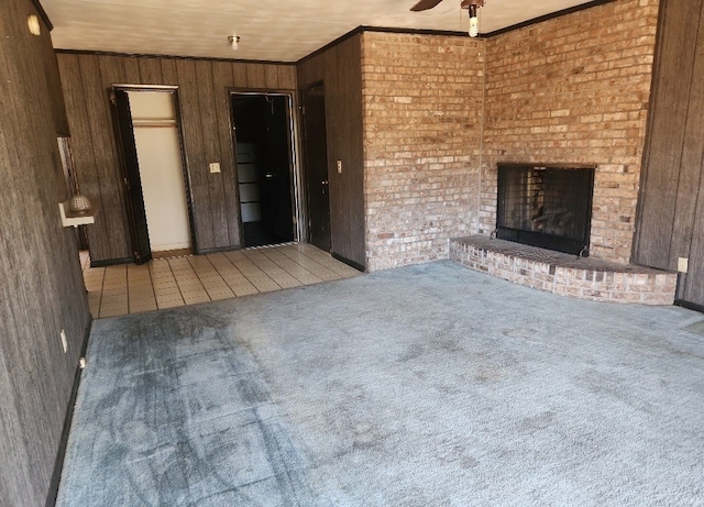 unfurnished living room with crown molding, wooden walls, carpet flooring, ceiling fan, and a fireplace