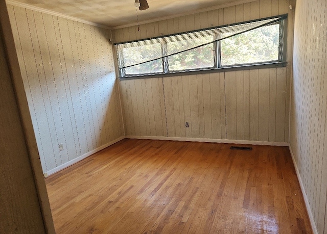 spare room with hardwood / wood-style floors, ceiling fan, crown molding, and wooden walls