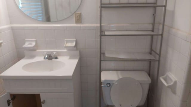 half bathroom featuring vanity, tile walls, toilet, and wainscoting