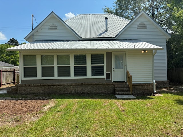 rear view of property featuring fence, a yard, entry steps, and metal roof