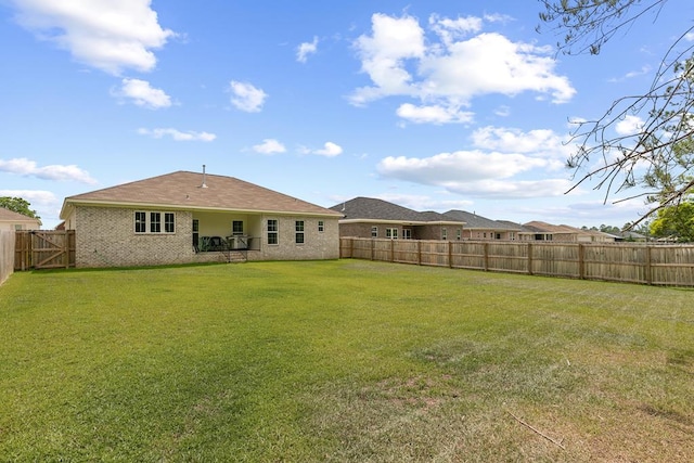 rear view of house with brick siding, a fenced backyard, and a yard