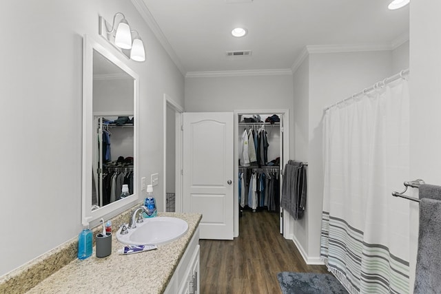 bathroom featuring a walk in closet, ornamental molding, wood finished floors, and visible vents