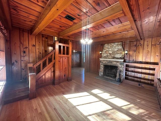 unfurnished living room featuring beam ceiling, wooden ceiling, a chandelier, light hardwood / wood-style floors, and a stone fireplace