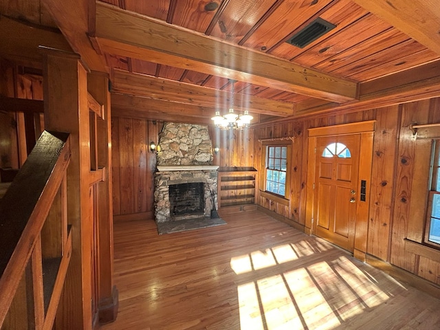 unfurnished living room featuring wood walls, wooden ceiling, light hardwood / wood-style floors, a fireplace, and beam ceiling