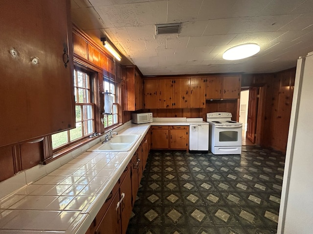 kitchen featuring white appliances, tile countertops, wood walls, and sink