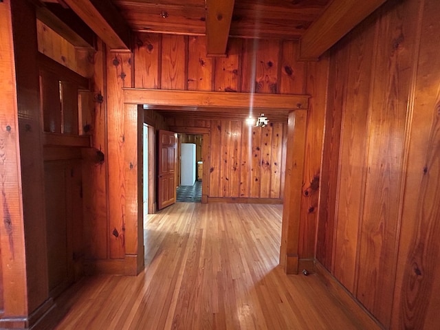 hallway with wood walls, beamed ceiling, and light wood-type flooring