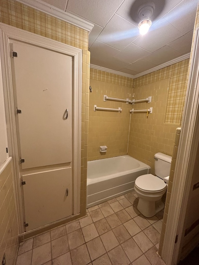 bathroom with tile patterned floors, shower / washtub combination, toilet, ornamental molding, and tile walls