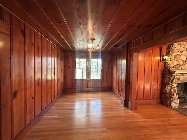 empty room with a fireplace, light hardwood / wood-style floors, wooden ceiling, and wood walls