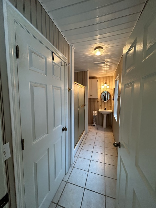 hallway featuring wood walls, light tile patterned flooring, and sink