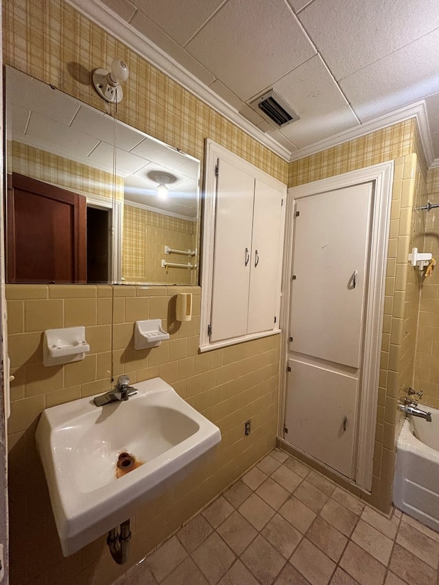 bathroom with tile patterned floors, ornamental molding, tub / shower combination, sink, and tile walls