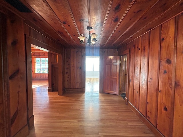 hall featuring light hardwood / wood-style floors, an inviting chandelier, wood ceiling, and wood walls