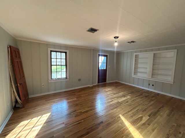 empty room with hardwood / wood-style floors, built in features, and ornamental molding