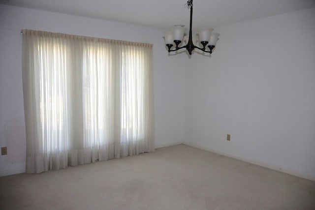 carpeted spare room featuring plenty of natural light and a chandelier