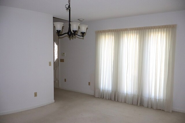 unfurnished room with light carpet, a wealth of natural light, and a notable chandelier