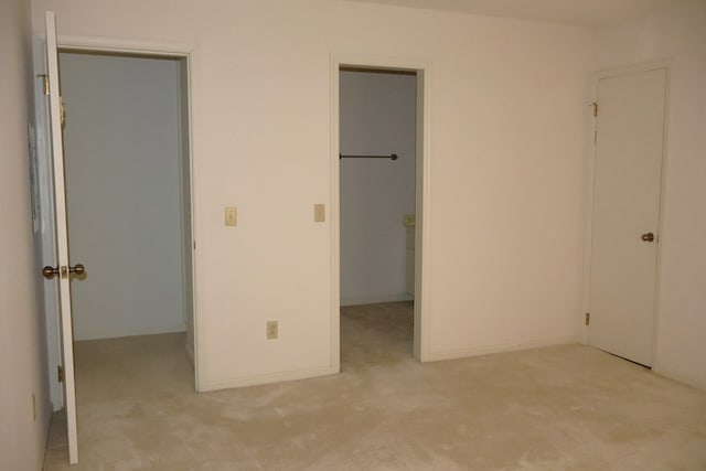 unfurnished bedroom with a walk in closet, light colored carpet, and a closet