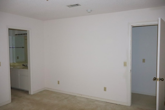 unfurnished bedroom with sink, ensuite bath, a spacious closet, a textured ceiling, and light colored carpet