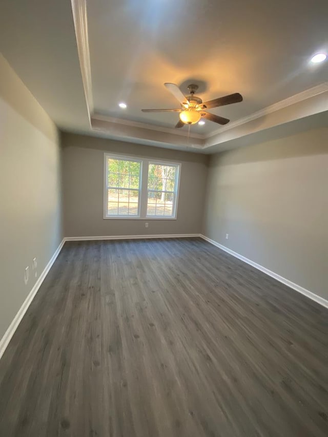 spare room with a tray ceiling, ceiling fan, dark wood-type flooring, and ornamental molding