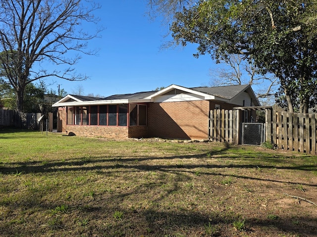 back of property featuring brick siding, fence, a sunroom, a lawn, and a gate