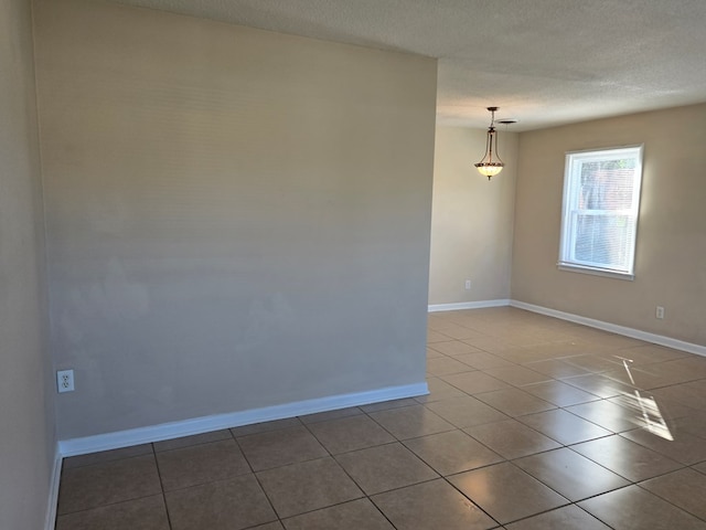 tiled empty room featuring a textured ceiling and baseboards