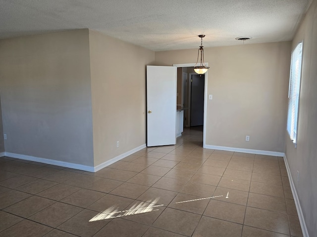 tiled empty room featuring visible vents, a textured ceiling, and baseboards